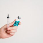 Hand holding a syringe and vaccine vial on a white background, symbolizing healthcare and immunization.