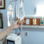 Close-up image of an IV drip and hand in a hospital room, illustrating medical care.